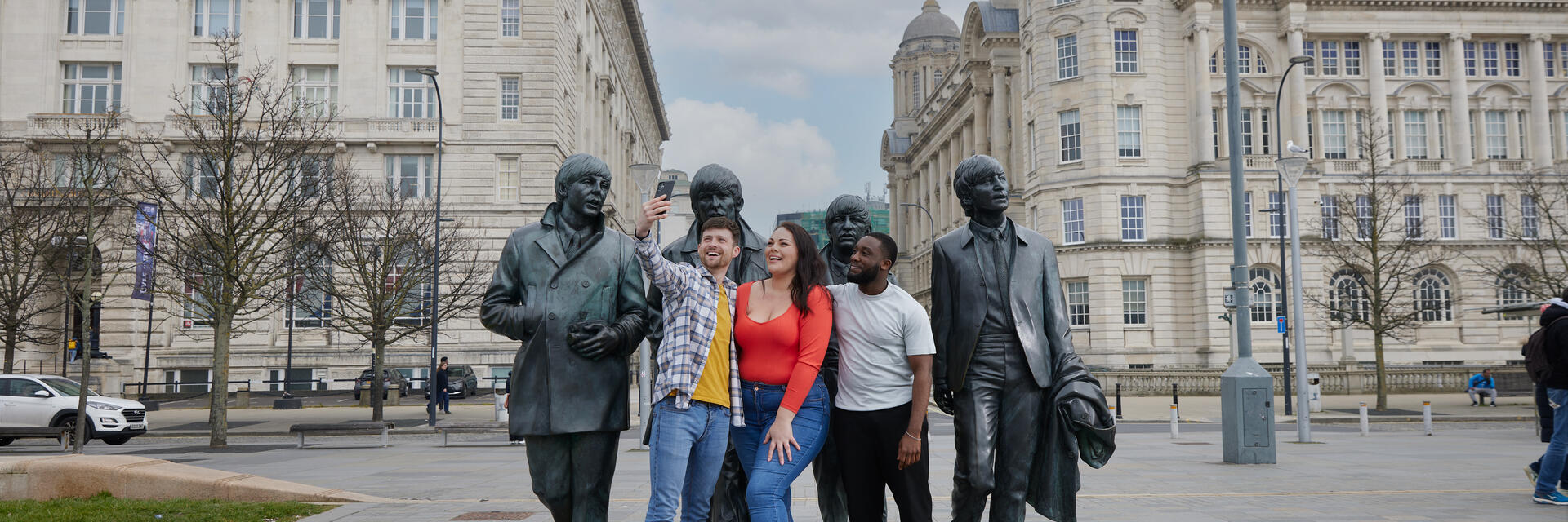 Eine Gruppe von Freunden, zwei Männer und eine Frau, machen ein Selfie vor einer Statue im Stadtzentrum.