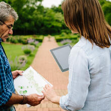 Man and woman sharing garden plans and designs stood on a path in a garden