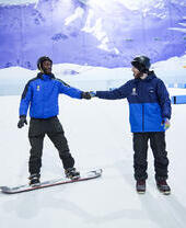 Two men skiing and snowboarding on an indoor snowslope at Chill Factore in Manchester