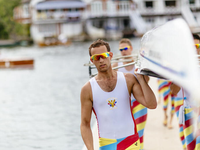 Rowers carrying a racing scull by the side of a river