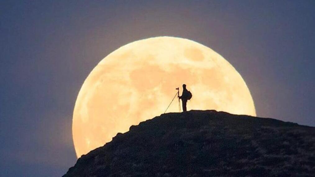 Person standing on hillside with a large moon in the background