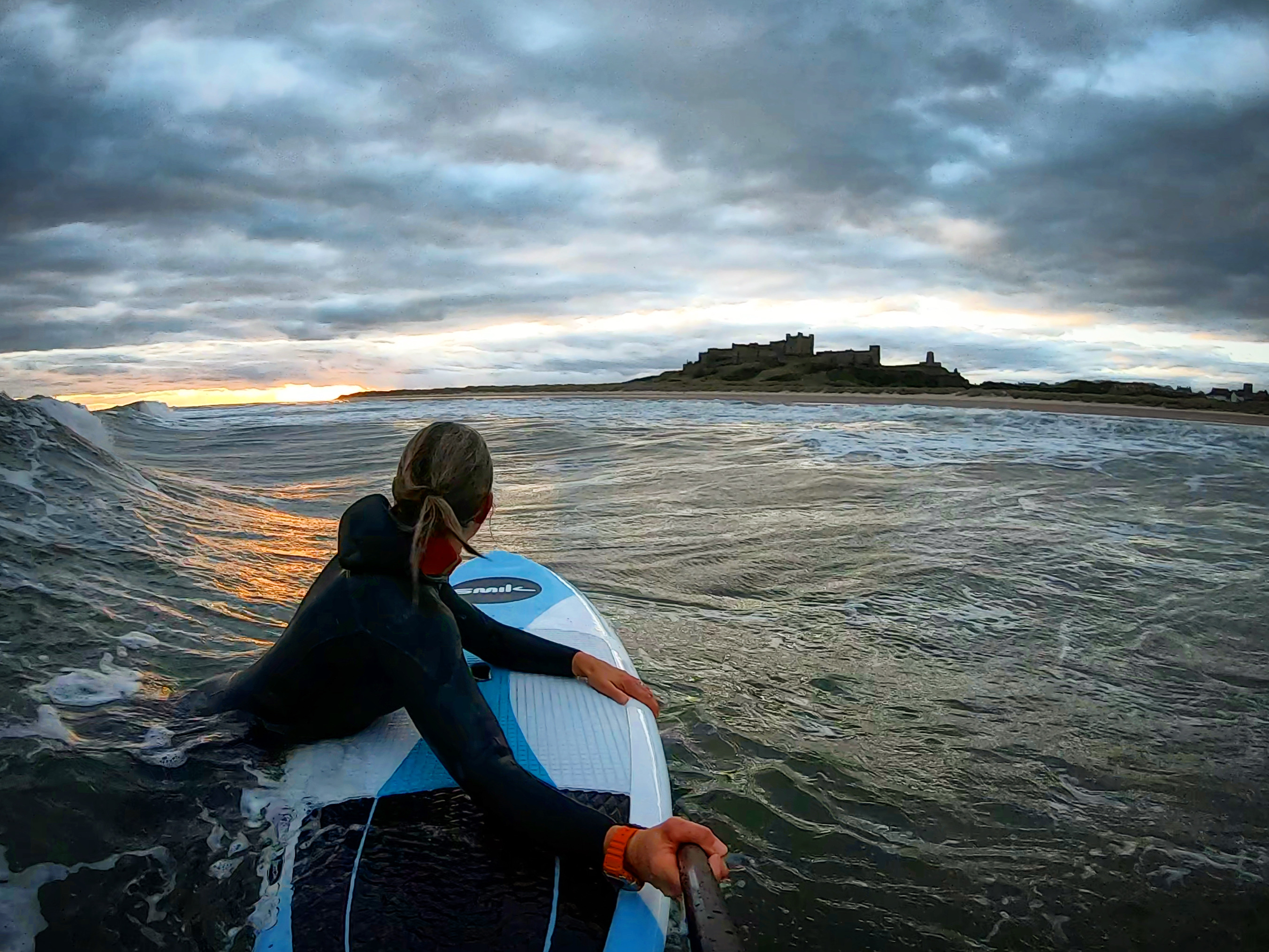 Woman in the sea on a paddle board looking towards a castle