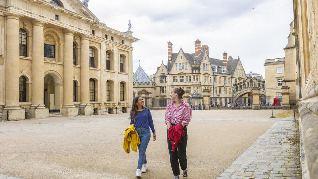 Zwei Frauen spazieren durch einen Innenhof zwischen historischen Gebäuden