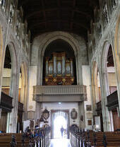 Intérieur d'une grande église avec des bancs en bois, des arches en pierre, un plafond en bois et un orgue à tuyaux au-dessus de l'entrée.