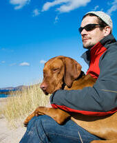 Uomo seduto con un cane ungherese vizsla in grembo sulla spiaggia isolata di Sandwood Bay in Scozia.