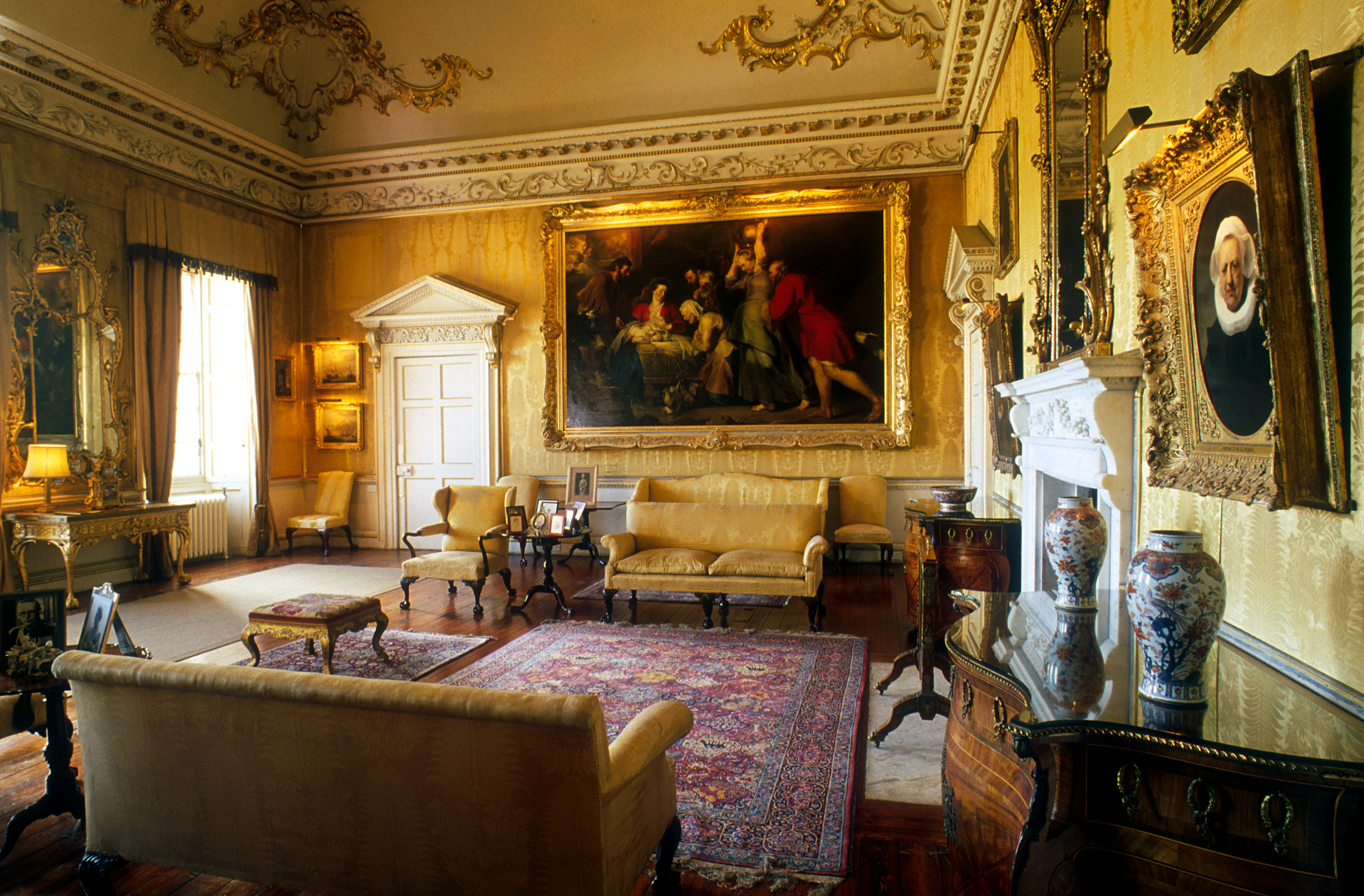 An ornate drawing room in a stately home with yellow walls, a red rug and other luxurious fittings.