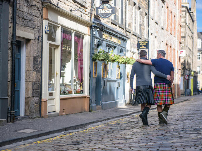 Gleichgeschlechtliches Paar, das Kilts trägt und Arm in Arm geht