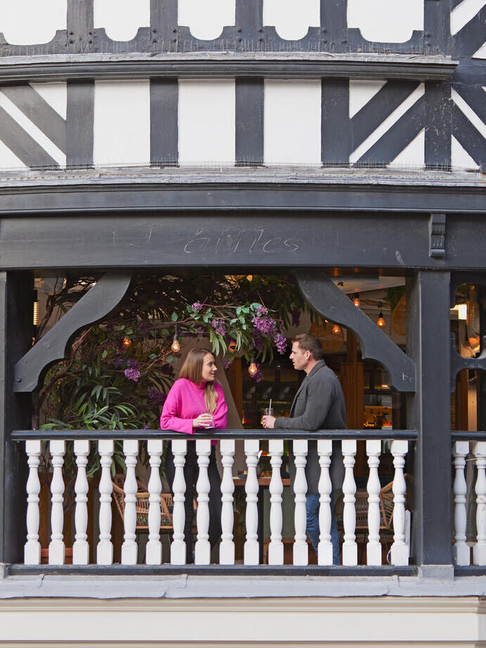 A man and a woman have a drink and talk on the balcony at a local cafe.