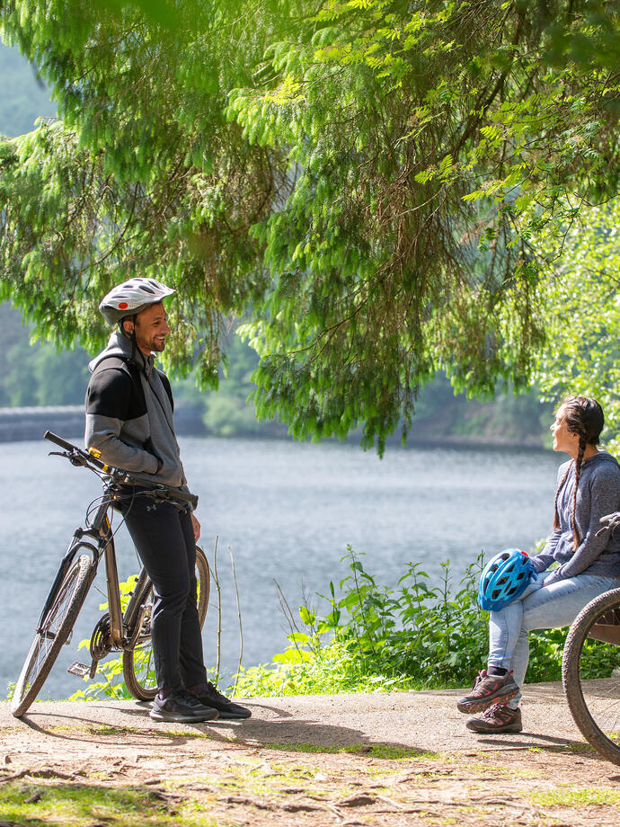 A man and a women take a rest from cycling by a reservoir
