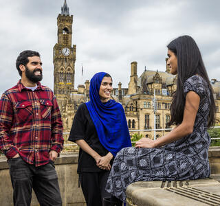 Two women and a man stand and talk in front of a town view