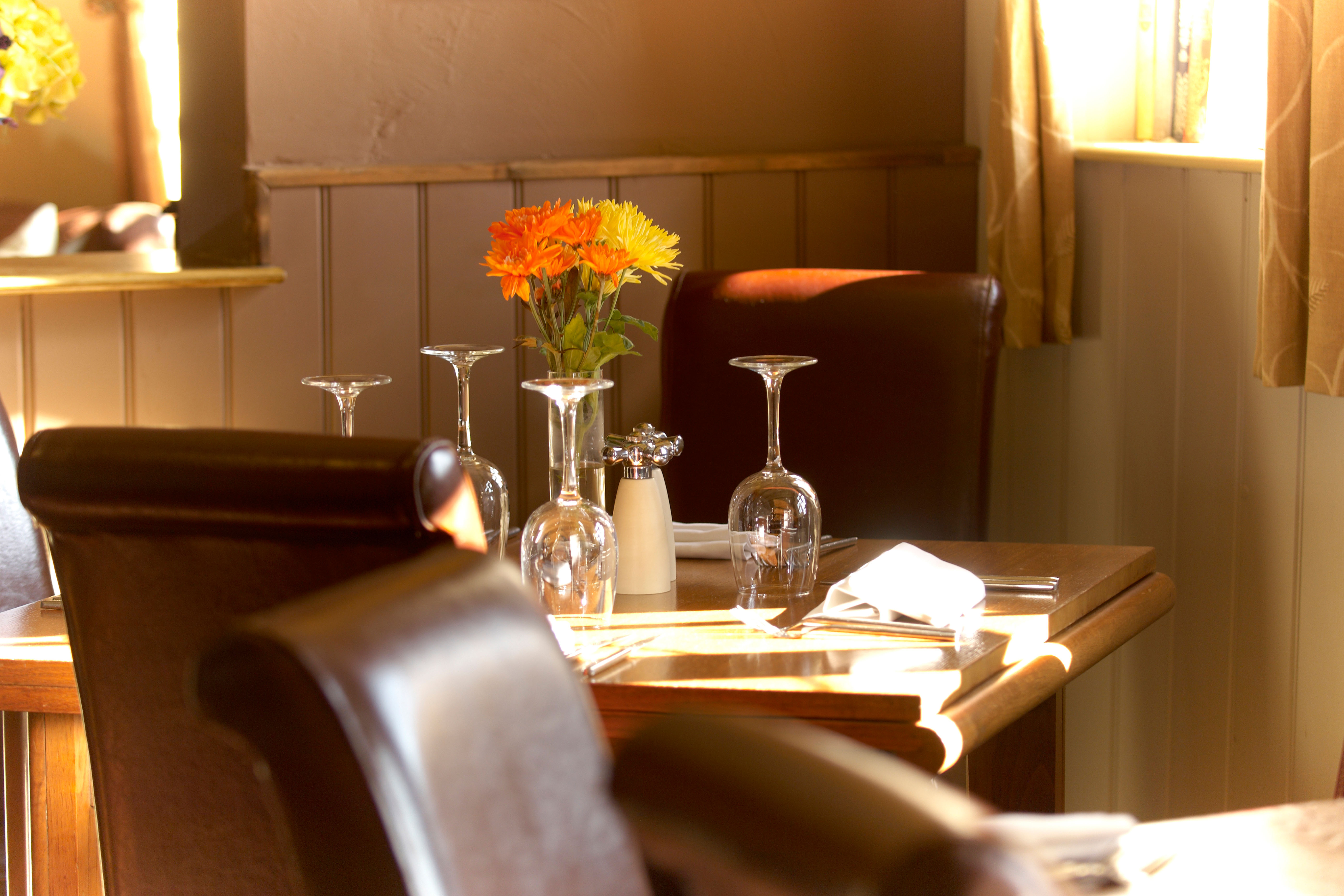Table de restaurant dressée avec des chaises en cuir, des verres et des fleurs.