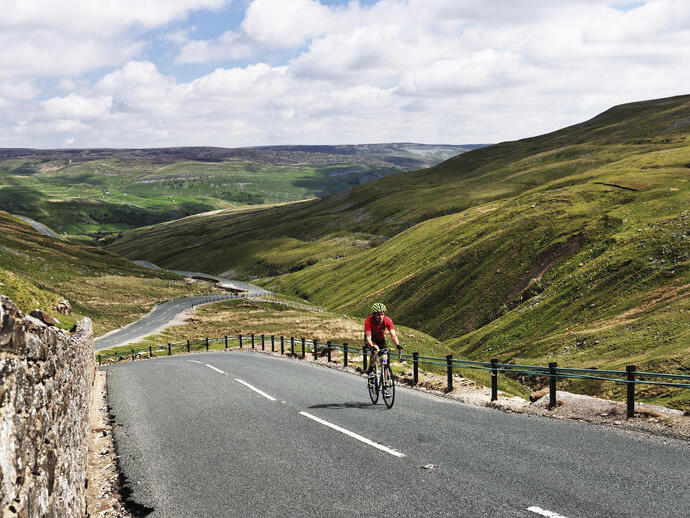 Cyclist riding on road through green dales