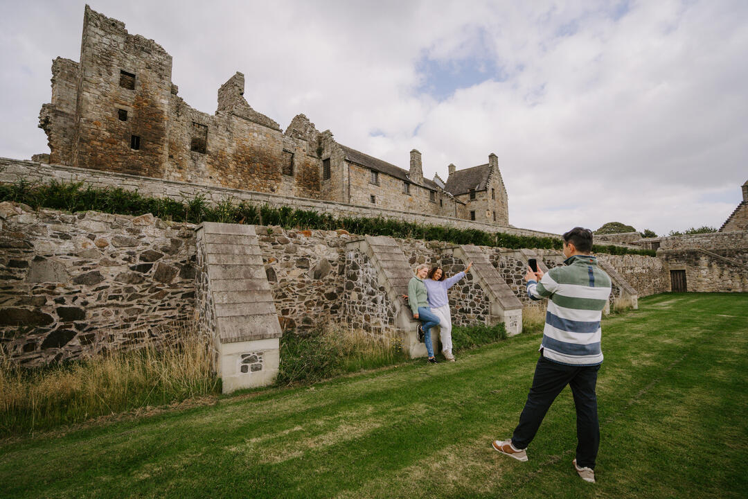 Tre persone scattano una foto davanti a rovine storiche in pietra su un prato.