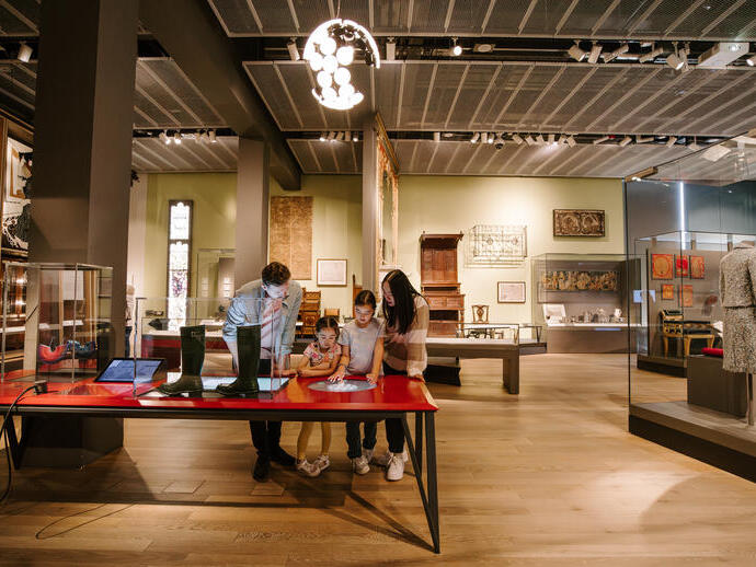 A man, a woman and two girls playing with touch screens inside a modern museum display.