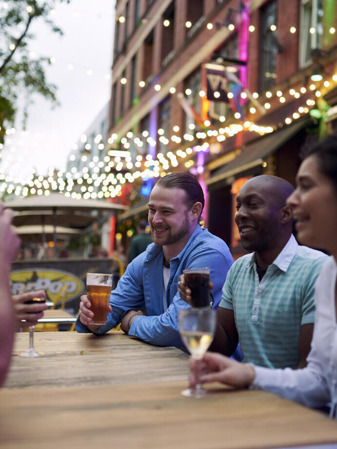 Friends having a drink sat at an outside table of a bar with fairy lights hanging behind