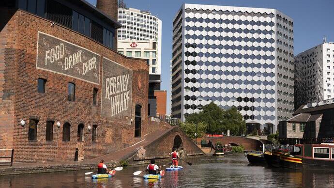 Group of people paddleboarding past industrial buildings on a canal