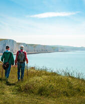 Two men hiking together with the stunning backdrop of white cliffs overlooking the ocean.