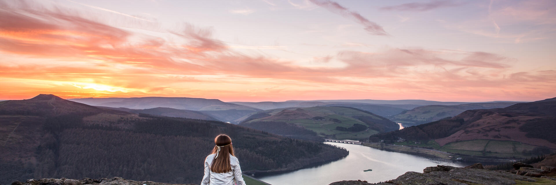 A woman sitting on rocks looking down valley to the river