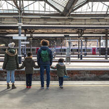 A multiracial family of four, a mother, father and their two little boys standing at Newcastle railway station platform waiting for their train.
