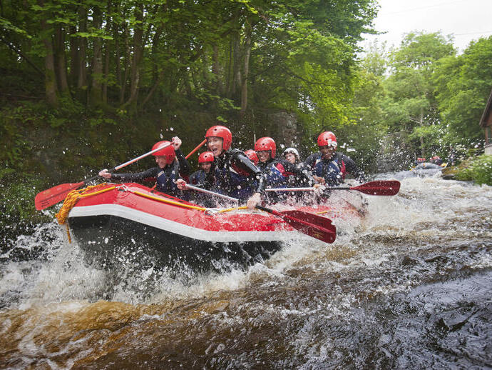 People wearing wetsuits and helmets paddling down a rapid