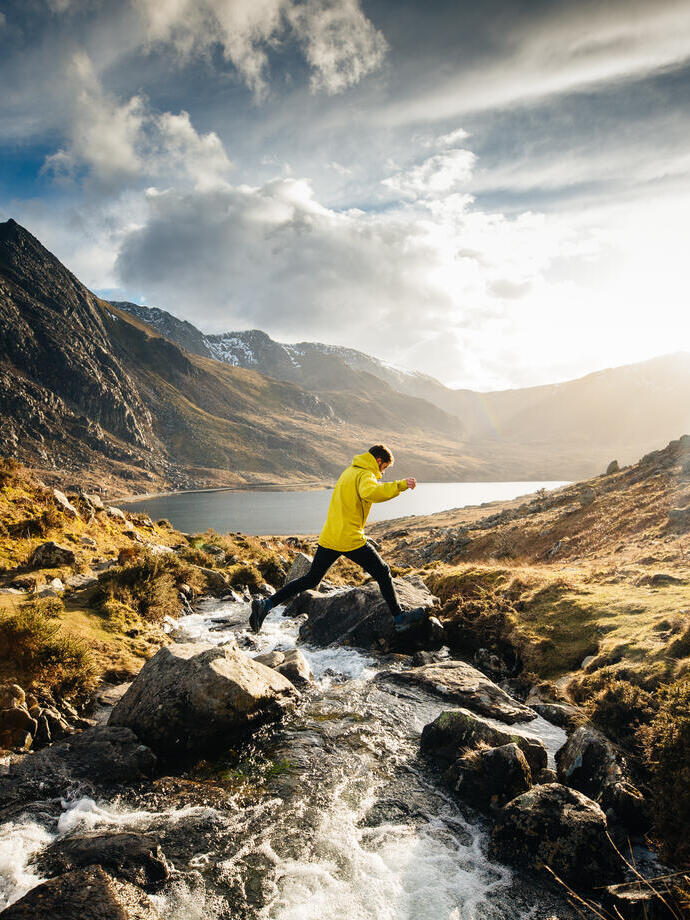 Man jumping from rock to rock across a stream flowing into a lake