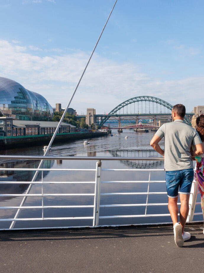 A family stand on ta bridge overlooking a city river.