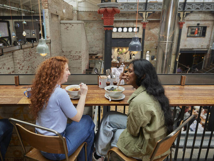 Two women enjoying lunch inside a large food hall.