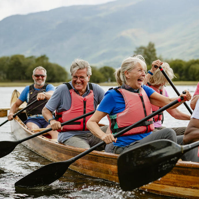 A senior group of friends wearing lifejackets enjoying rowing in a single boat on a river.
