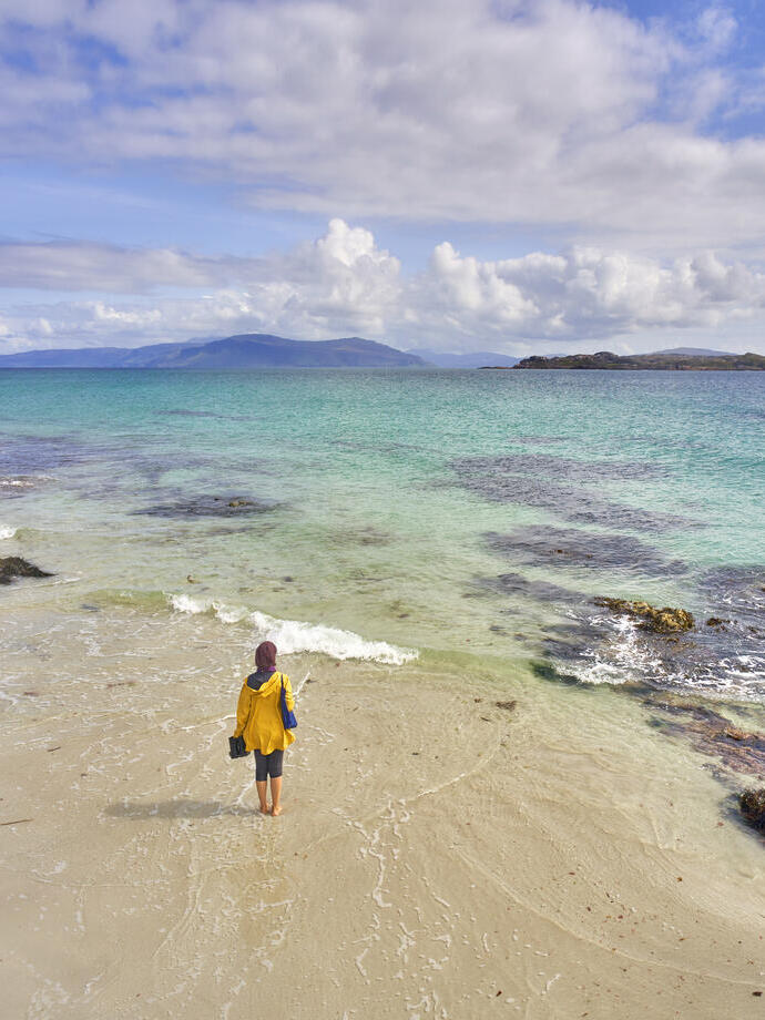 Eine junge Frau, die auf dem weißen Sandstrand mit kristallklarem, blauem Wasser spazieren geht.