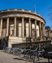 Historic circular building with columns, a flag on top, bicycles parked outside, and a tree visible to the right.