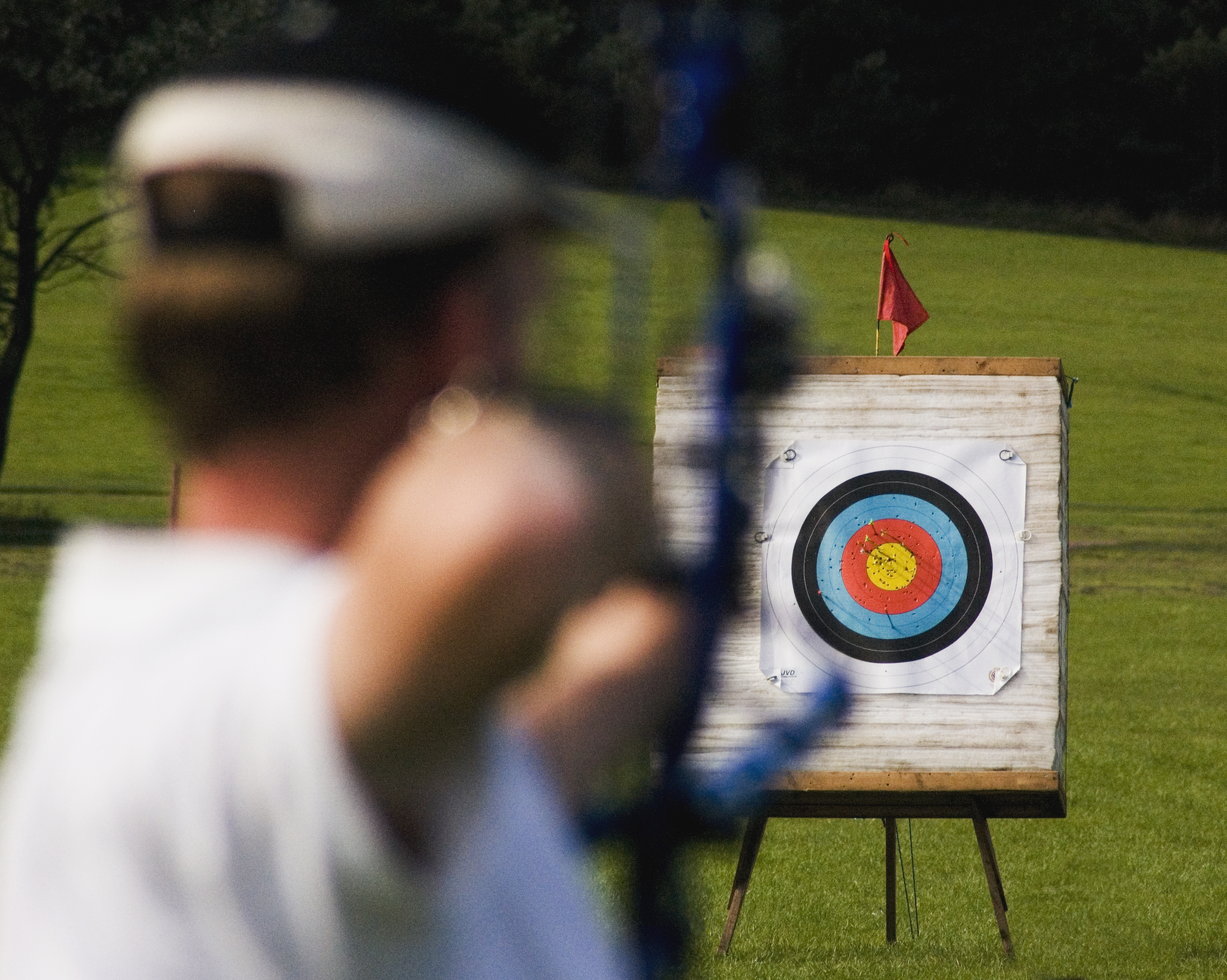 A person aiming a bow and arrow at a target from distance.