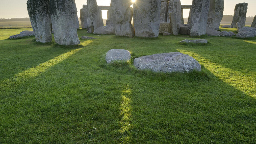 Grandes pilares de piedra dispuestos en círculo sobre la hierba. Puesta de sol