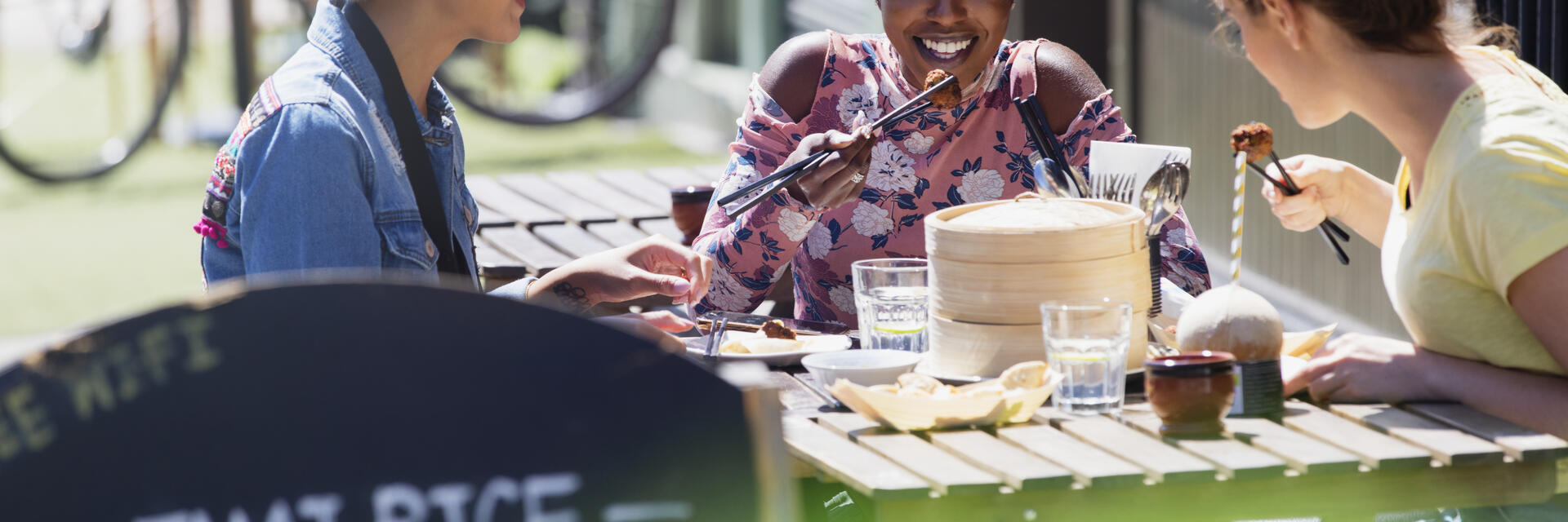 Drei junge Freundinnen genießen ein Dim-Sum-Mittagessen in einem sonnigen Straßencafé