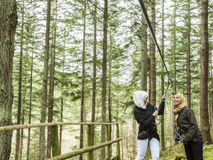 Two women preparing to go on a zipwire in the pine forest