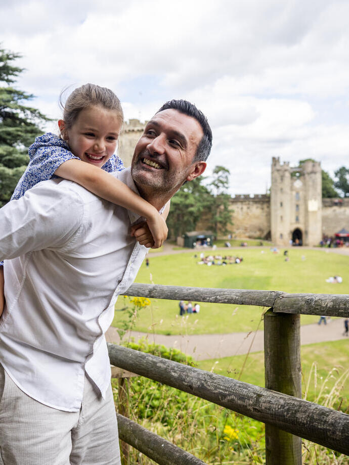 A man holds his daughter on his back in front of a heritage castle