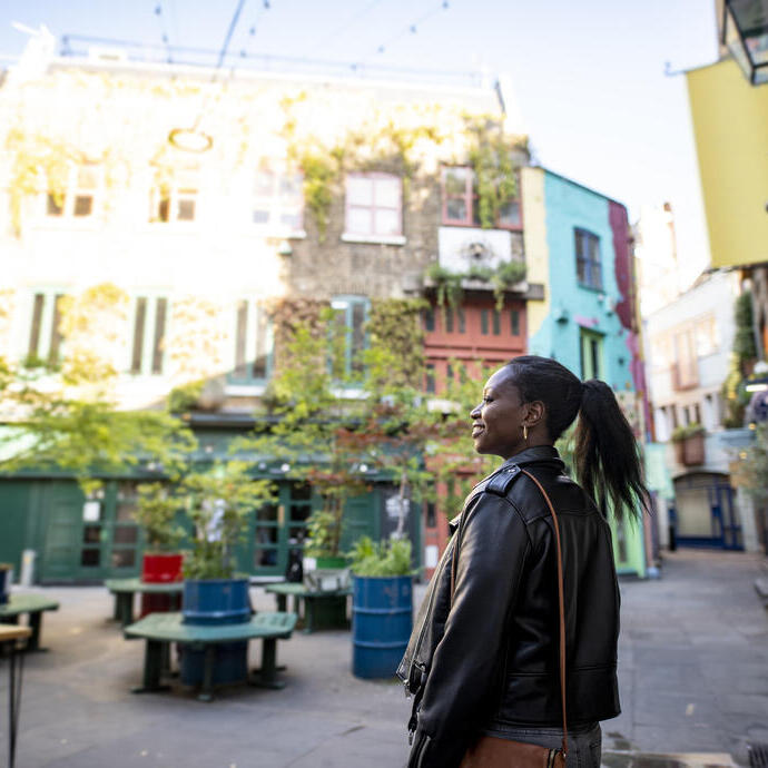 Female tourist exploring a London shopping courtyard with shops and outdoor seating.