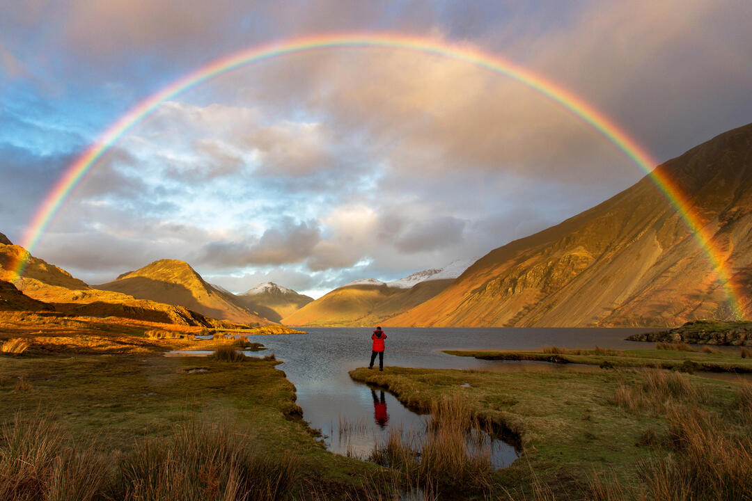 Man standing on the edge of a lake watching a rainbow