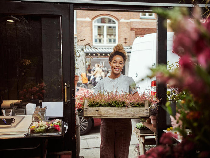 Young woman entering her flower shop carrying a tray of heather plants