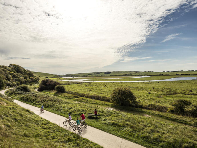 A family cycling along path through the wide open grassy English landscape.