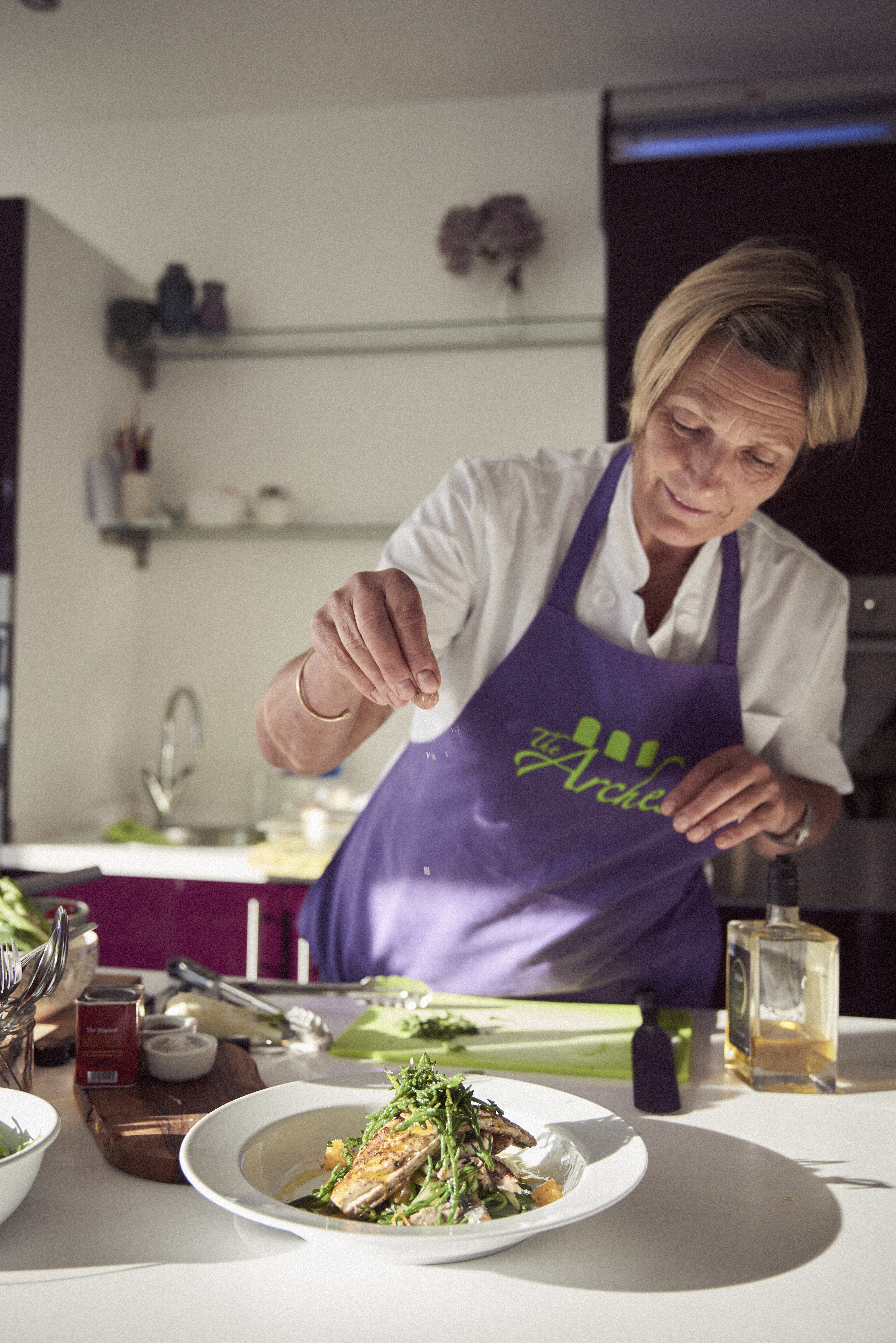 Mujer rubia con delantal morado preparando comida en la cocina