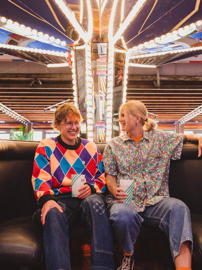 A man and a woman wearing roller skates sit in a retro teacup at a roller disco