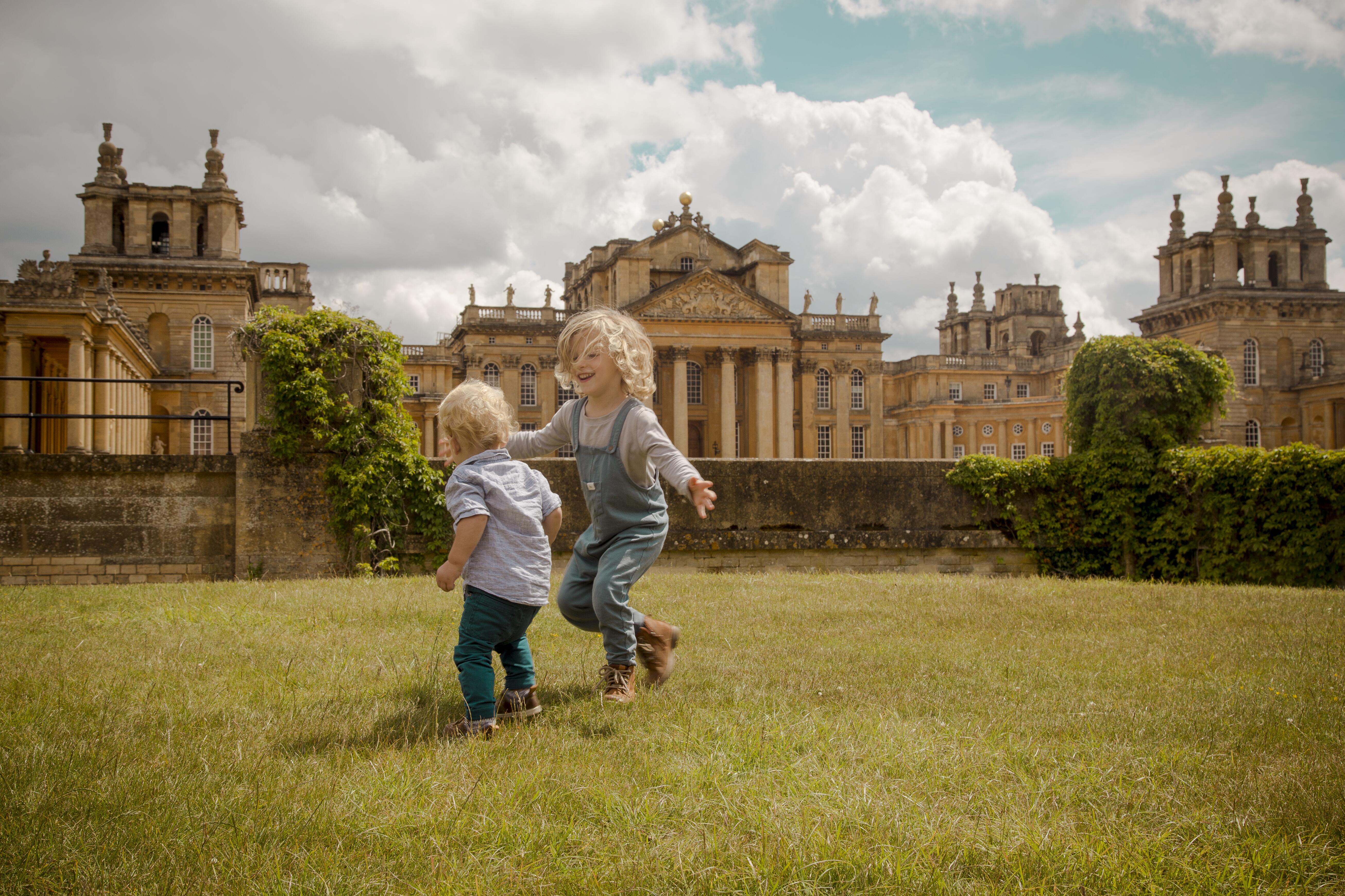 Two children play on the lawn in front of a palace