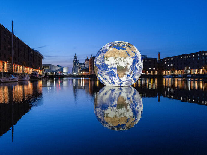 A sphere earth artwork floating in the middle of the docks surrounded by buildings and lit up at night