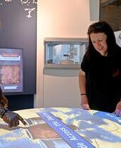 Three people interact with a large touchscreen display map in a modern museum, engaging with educational content about the Roman Empire.