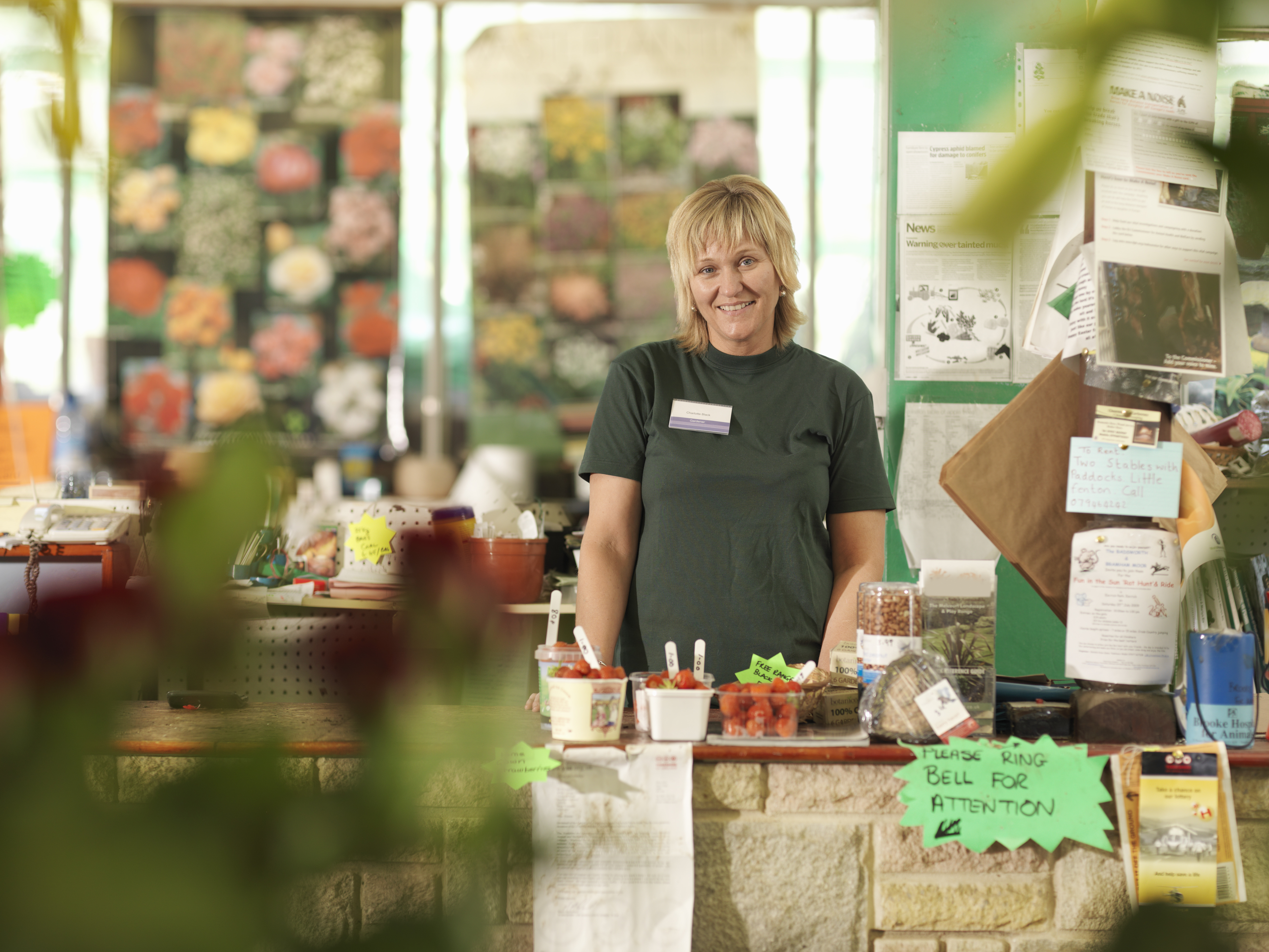 Una trabajadora del centro de jardinería con delantal detrás de la caja registradora.