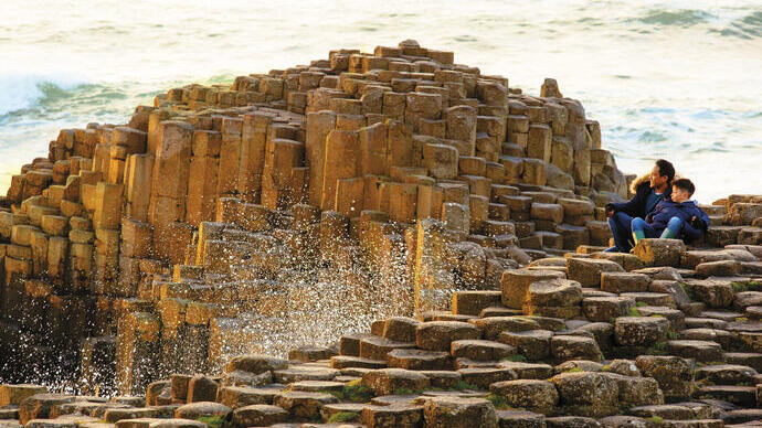 Man and child sitting on rock formations by the sea