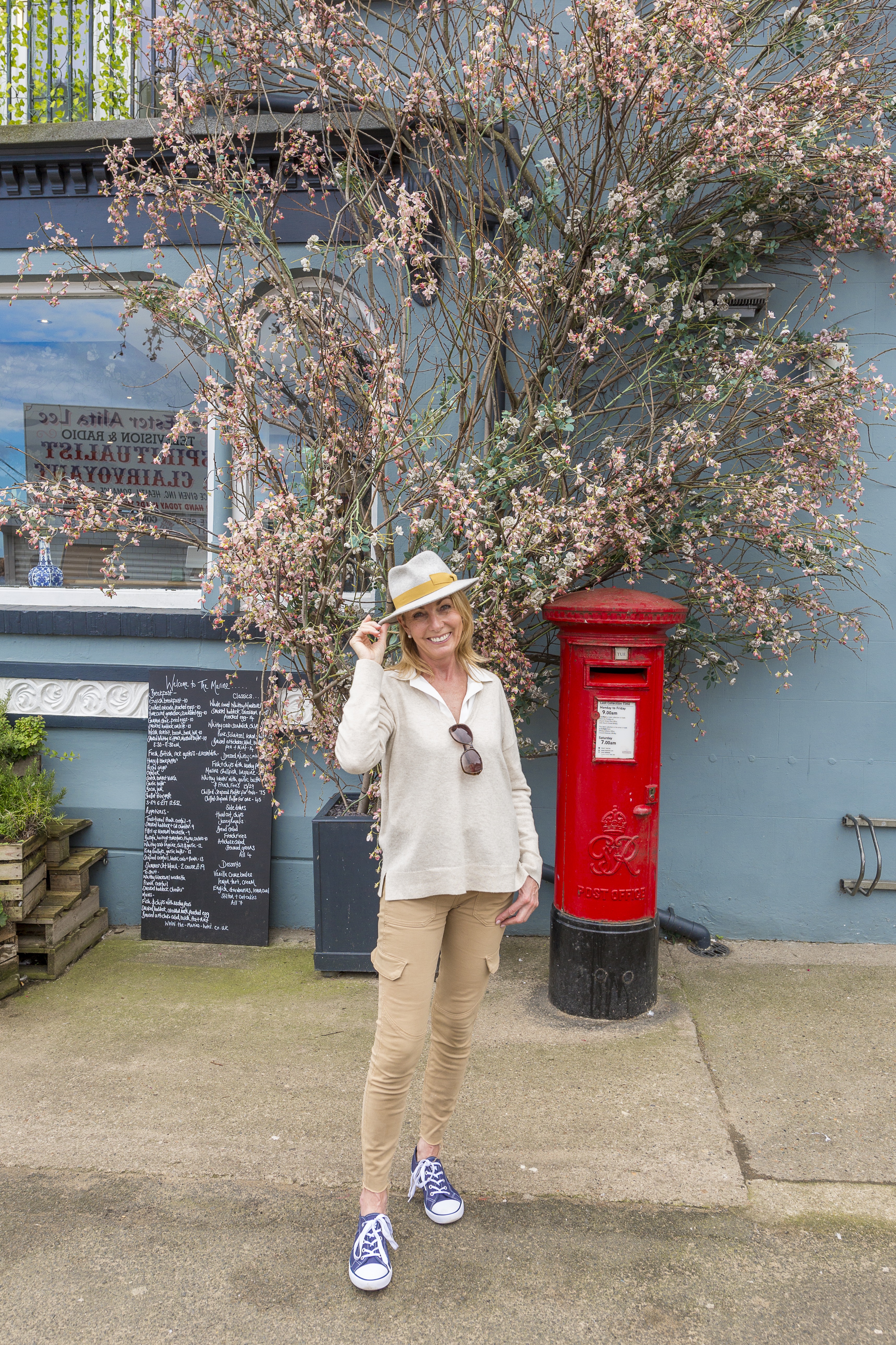 Mujer con sombrero junto a un buzón y un árbol en flor en un hotel