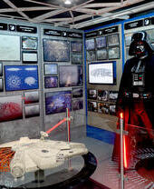 An actor in a Dath Vader costume in a Star Wars themed exhibit.