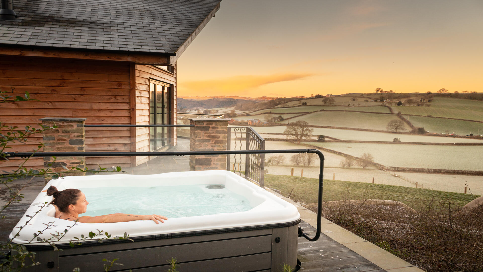 A woman in an outdoor Hot Tub,looking out across rolling farmland in the morning mist.