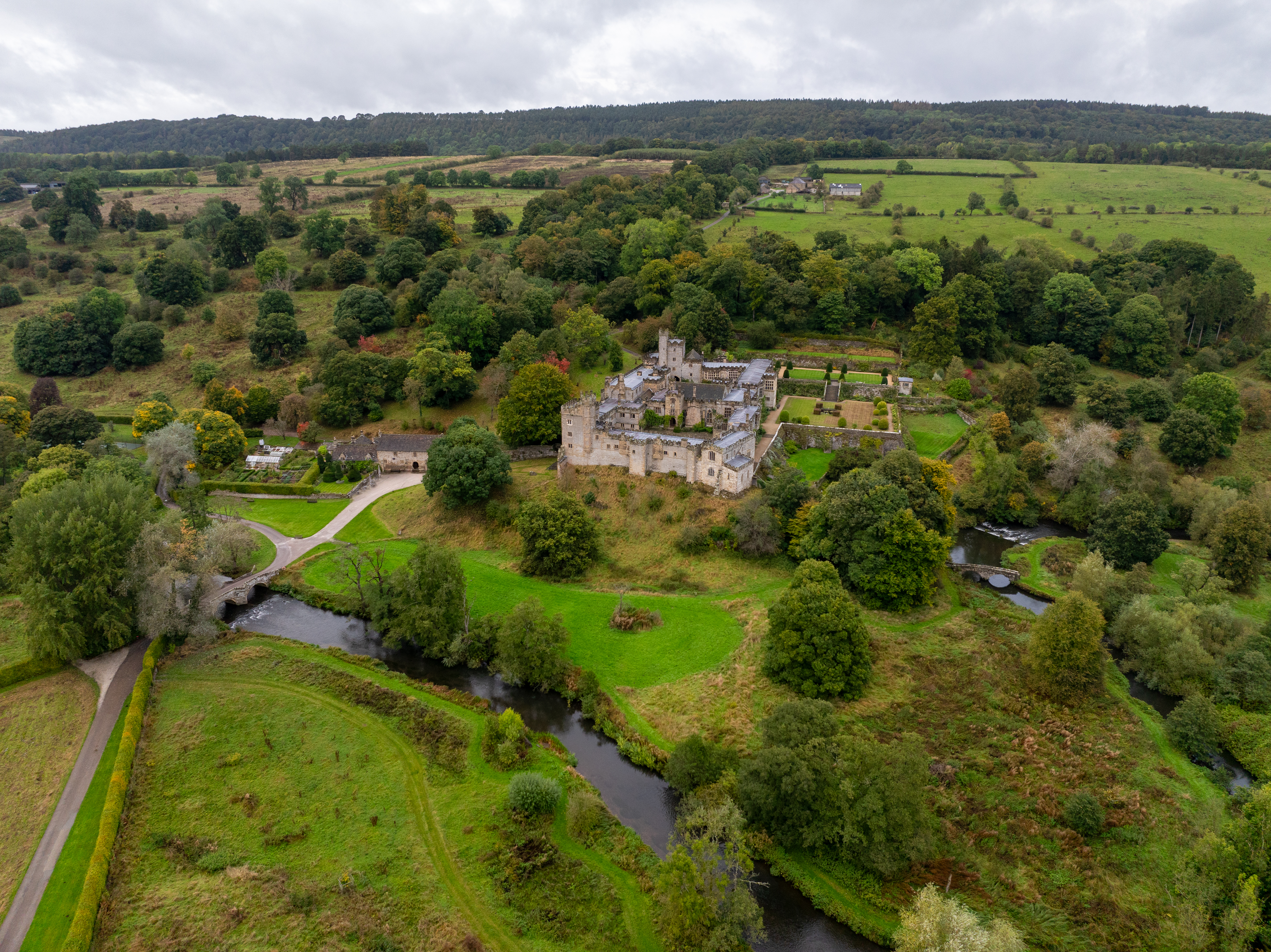Aerial view of large manor house surrounded by green fields, trees, and a river in the countryside